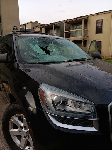 Black SUV with severely damaged windshield in apartment parking lot